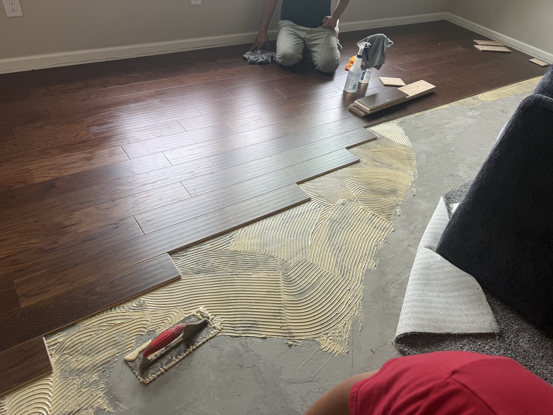 Installer setting hardwood plank flooring with adhesive during a Four Pillars installation